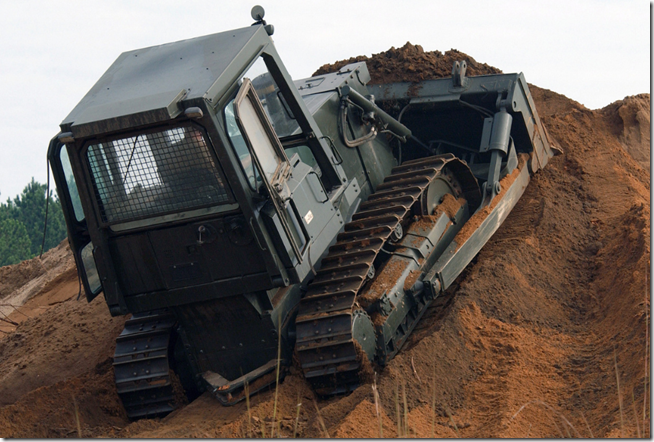 Bulldozer climbing a mound of dirt.